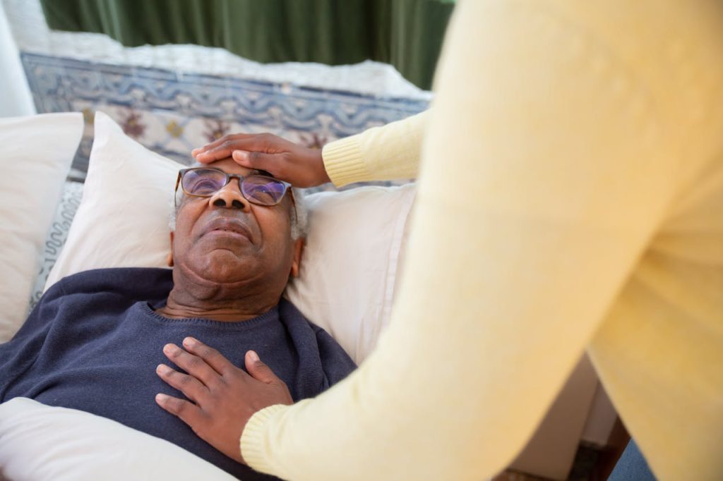 A caregiver attending to an elderly man in bed, providing comfort and support.